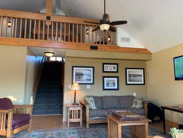 A spacious living room with a high ceiling, wooden staircase, and a ceiling fan.