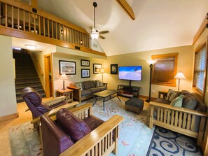 A spacious living room with a wooden staircase, a flat-screen TV, and a comfortable seating area with leather chairs and a sofa.