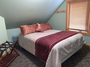 A bedroom with a bed, pillows, a blanket, a wooden ladder, and a window with blinds.