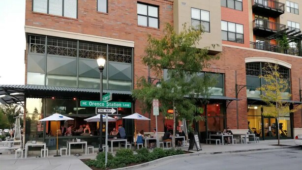 A restaurant with outdoor seating, a street sign, and a building with a brick facade. - Modern home in Orenco (Hillsboro)