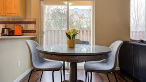 A dining area with a glass table and two chairs, a vase with flowers, and a view of a backyard through a sliding glass door. - Modern home in Orenco (Hillsboro)