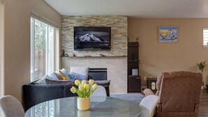 A living room with a stone fireplace, a flat-screen TV mounted above it, a sofa with cushions, a glass coffee table with a vase of tulips, and a painting on the wall. - Modern home in Orenco (Hillsboro)
