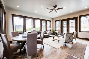 A spacious living room with a dining area, large windows, and a ceiling fan.