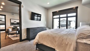 Un dormitorio con cama, cómoda, televisor y un ventanal grande.