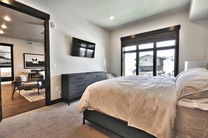Un dormitorio con cama, cómoda, televisor y un ventanal grande.