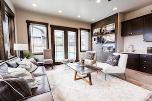 A spacious living area with a sofa, armchairs, and a coffee table. There are large windows providing a view of the outside. - Blackstone 2BR/2.5BA | Two King Suites | Pool & Hot Tub | Canyons Village (Park City)