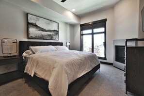 Une chambre moderne avec un grand lit, une table de chevet, un bureau, une chaise, une cheminée et une grande fenêtre donnant sur un beau paysage.