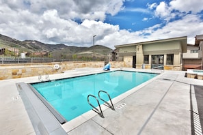 A swimming pool with a stone wall and a metal ladder, surrounded by a fenced area with a mountain view in the background. - Blackstone 2BR/2.5BA | Two King Suites | Pool & Hot Tub | Canyons Village (Park City)