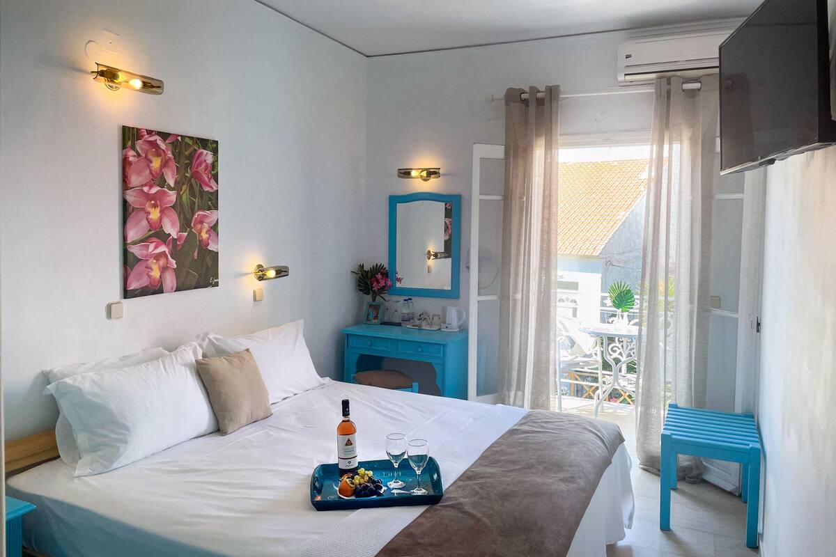 Quarto de hotel com cama, mesa de cabeceira, cômoda, espelho e janela com cortinas.