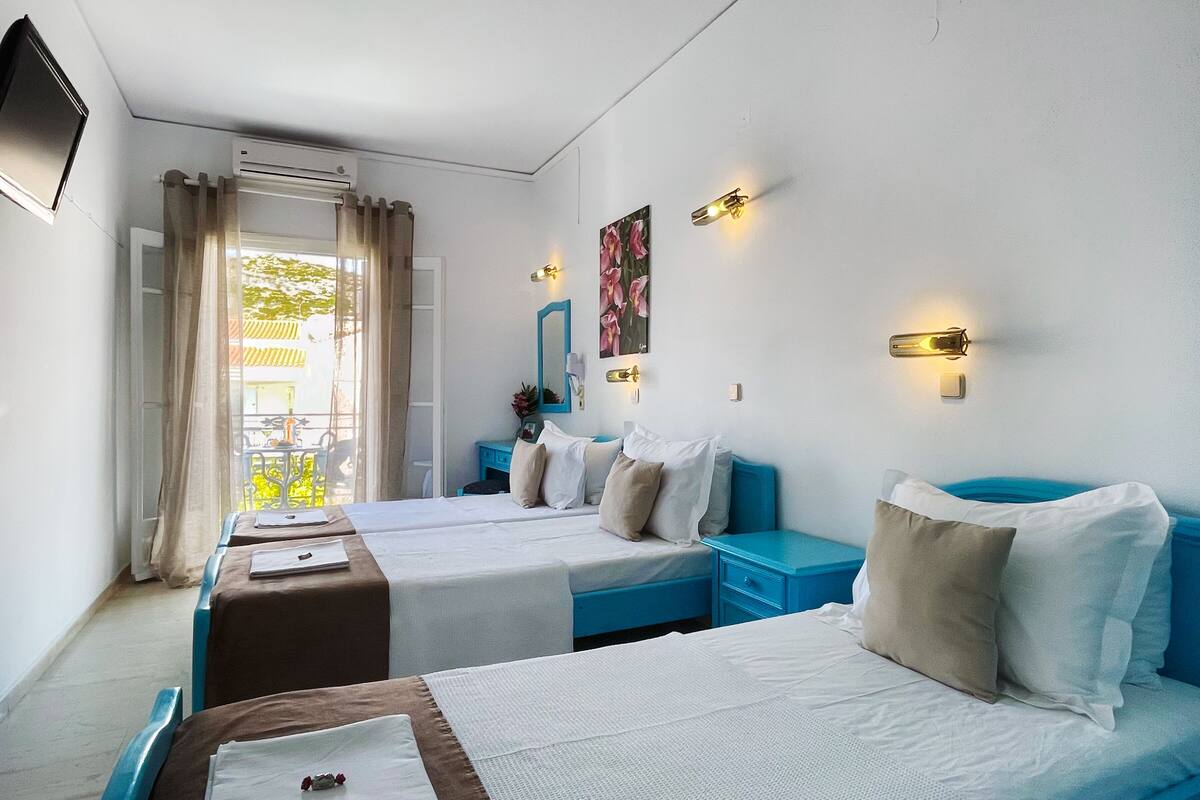Quarto de hotel com duas camas, televisão, ar condicionado e varanda com cortinas.