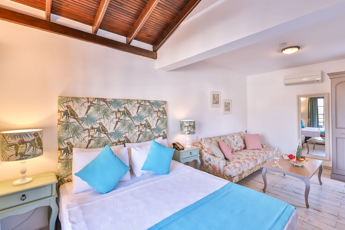 A hotel room with a bed, a sofa, a nightstand, a table, and a mirror.