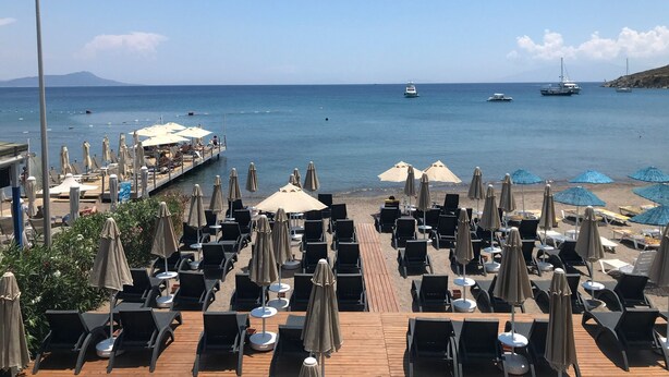A beachside restaurant with outdoor seating, a wooden deck, and a view of the sea and boats. - Mare Garden Hotel Akyarlar (Bodrum)