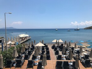 A beachside restaurant with outdoor seating, a wooden deck, and a view of the sea and boats. - Mare Garden Hotel Akyarlar (Bodrum)