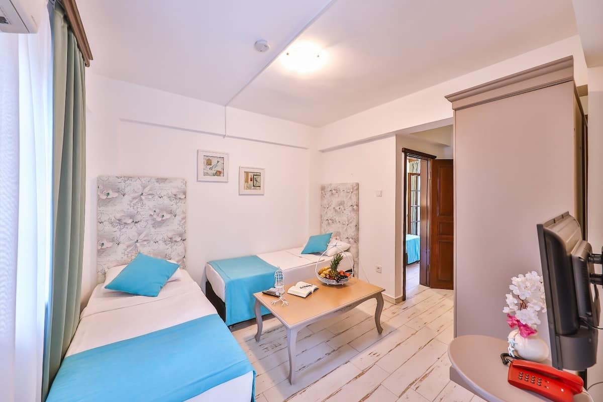 A hotel room with two beds, a small table with a basket of fruit, a TV, and a door leading to another room.