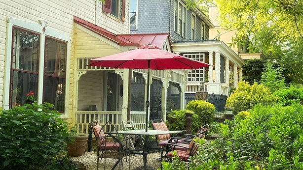A covered patio with a table and chairs, surrounded by lush greenery and a house with a porch. - Whole House Rental in Virgina (Lynchburg)