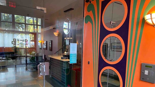 A hotel lobby with a glass door entrance, a reception desk, and a view of the outdoor seating area. - Right on the Beach Ocean Dr Secured Condo 206 (Miami Beach)