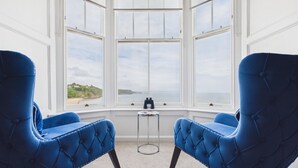 Una habitación con dos sillas azules orientadas hacia un ventanal con vistas a la costa.