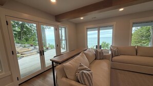 Ein modernes Wohnzimmer mit einer Eckcouch, einem Holztisch und großen Fenstern mit Blick aufs Meer.