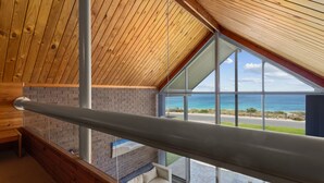 Interior moderno com teto de madeira, parede de vidro e vista para o oceano.
