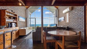 Um interior acolhedor com parede de tijolos, móveis de madeira, área de refeições e vista para o oceano.