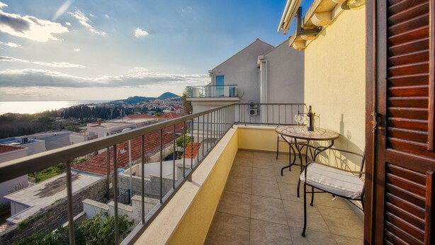 A balcony with a table and chairs, overlooking a cityscape and the sea.