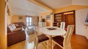 A spacious living area with a sofa, dining table, and chairs, a kitchen area with cabinets and a TV, and a door leading to another room.