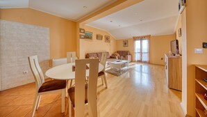 A spacious living area with a dining table and chairs, a sofa, and a television.