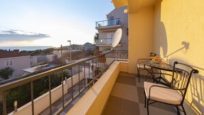 Un balcón con mesa y sillas, una antena parabólica y vistas al mar y edificios.