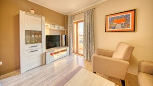 Un salón con televisor, sofá, aparador y un cuadro en la pared.