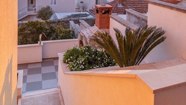 Edificio residencial con vista al mar al atardecer, una escalera y un balcón con plantas.