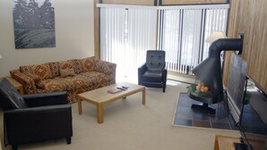 A living room with a sofa, two armchairs, a coffee table, a fireplace, and a large window with blinds.