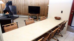 A long dining table with six chairs, a television on a stand, and a fireplace.