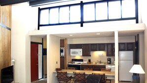 A modern kitchen with a central island, a dining area with chairs, and a television in a corner.