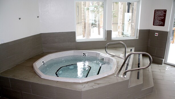 A hot tub with a metal ladder, a window with a view of trees, and a sign on the wall.