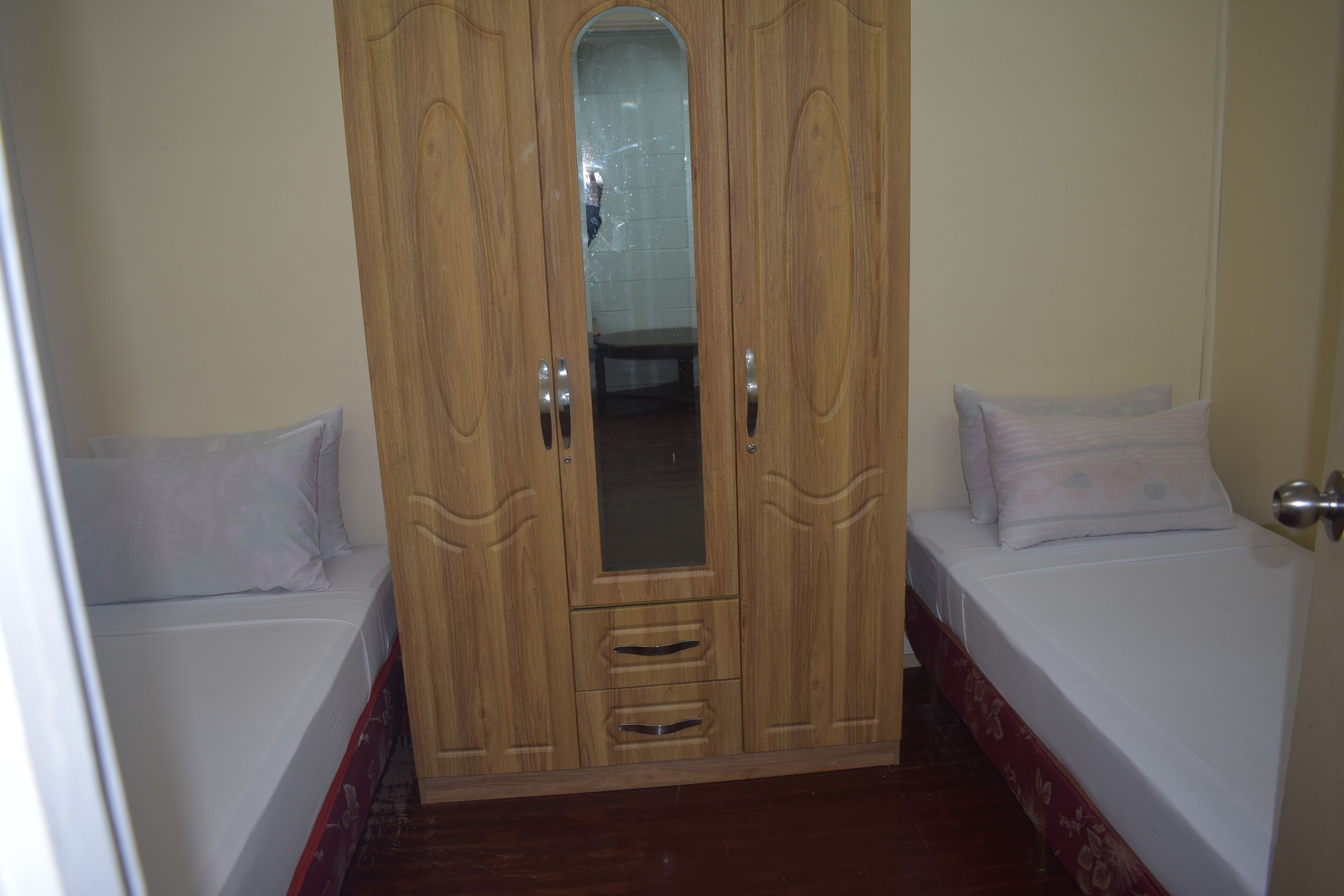 A bedroom with a wooden wardrobe, two single beds, and a mirror.