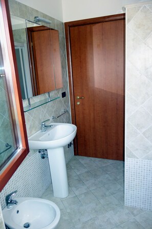 Un baño con un lavamanos blanco de pedestal, un estante de vidrio arriba y una puerta de madera.