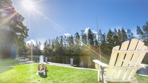 Escena junto al lago con un perro, una silla de madera y una caña de pescar.