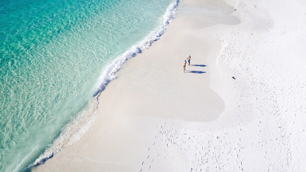 Vista aérea de una playa con aguas turquesas cristalinas y arena blanca.