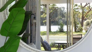A view through a window with a view of a lake, a white fence, and greenery. - Calm Waters Waterfront Cottages @ Sussex Inlet, No. 2 Waterfront (Sussex Inlet)