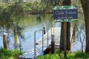 Um cais com uma placa indicando 'Cali Waters Guest Use Only' em um ambiente natural com árvores e água.