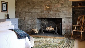 Una chimenea de piedra con repisa, un cuadro enmarco y una silla de madera.