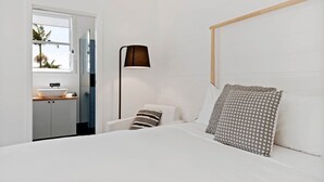 A bedroom with a bed, a bedside table, a lamp, a window, and a view of the outside. - Studio Ocean Breeze @ Huskisson (Huskisson)