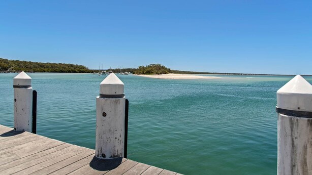 A wooden dock with two white bollards, a clear blue sky, and calm turquoise water. - Studio Ocean Breeze @ Huskisson (Huskisson)