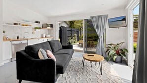 A modern living room with a black sofa, a small wooden table, and a kitchen area with white cabinets and a microwave. - Studio Ocean Breeze @ Huskisson (Huskisson)