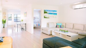 A modern living room with a sofa, coffee table, and a dining area with chairs and a table. - Ocean Breeze @ Huskisson (Huskisson)
