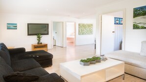 A modern living room with a black sofa, a white coffee table, and a television on the wall. - Ocean Breeze @ Huskisson (Huskisson)
