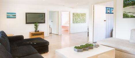 A modern living room with a black sofa, a white coffee table, and a television on the wall.