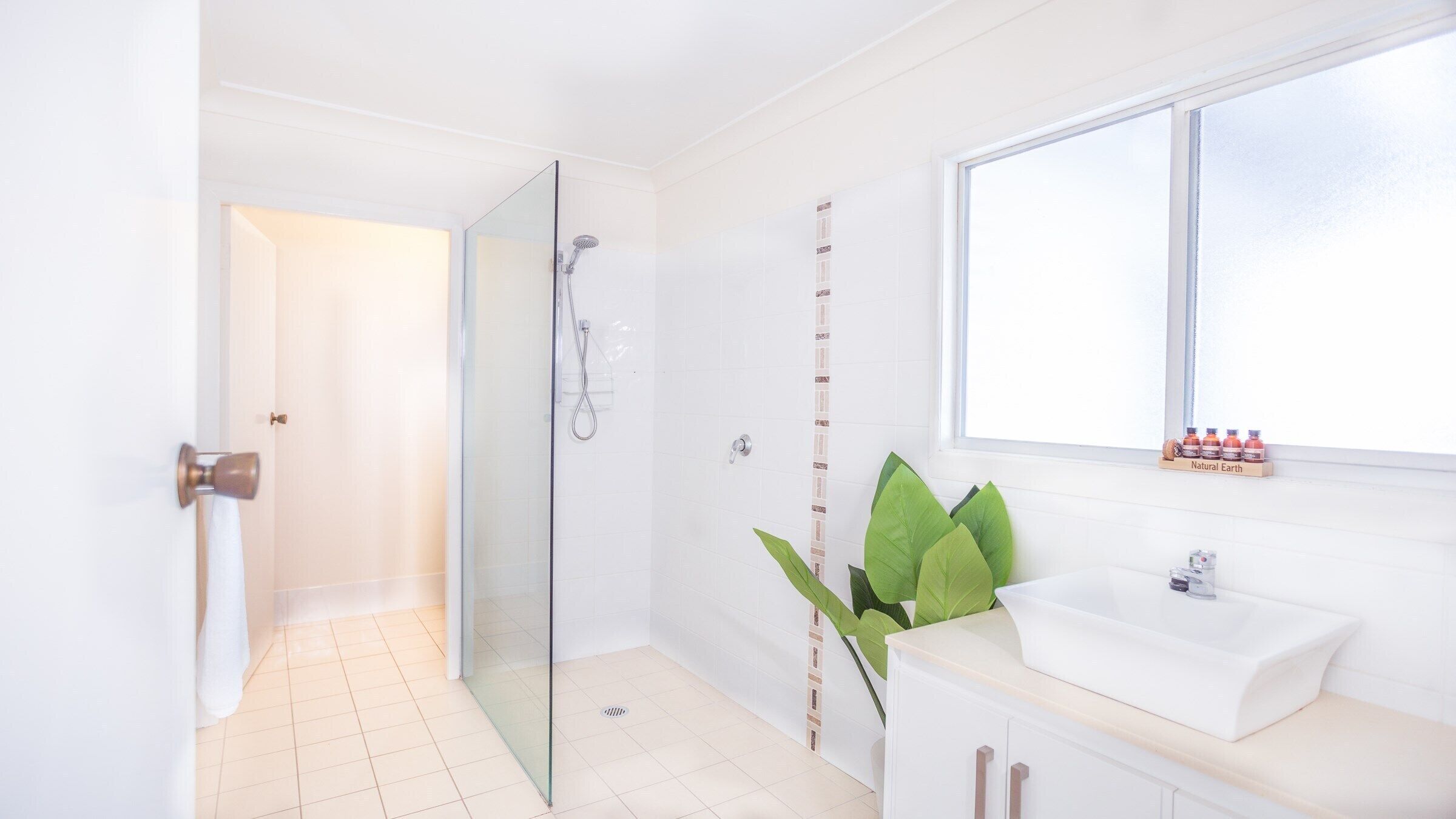 Une salle de bain moderne avec une douche à parois de verre, un lavabo blanc et une fenêtre offrant une belle vue.