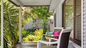 A covered outdoor seating area with a white chair and table, surrounded by lush greenery and a view of a residential building. - Ocean Breeze @ Huskisson (Huskisson)
