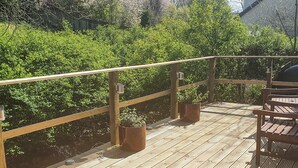 Una terraza de madera con barandilla, plantas en macetas y un banco.